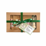 A holiday-themed gift set in a brown kraft paper box with a clear window, tied with a green ribbon and a hanging tag from 'Trul Teas'. Visible items include a christmas tree tea Infuser, a teaspoon, and 3 0.5oz of tea inside.