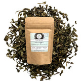 Brown paper bag of Truly Teas Organic Jasmine tea surrounded by loose tea leaves on a white background